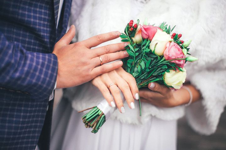 couple holding bouquet wedding rings