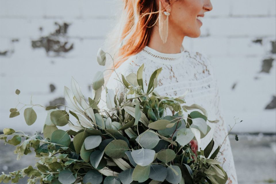 trendy bride wearing blue tulle skirt and lace crop top carries oversized presentation wedding bouquet with greenery