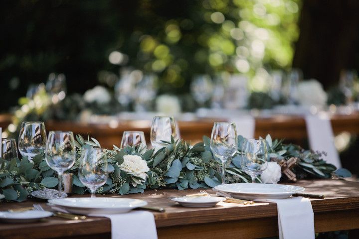 wedding reception tablescape with white plates, napkins and greenery centerpiece