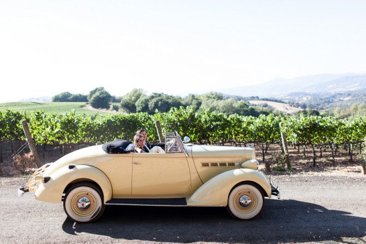 bride and groom sitting in vintage yellow convertible driving through Napa Valley vineyard