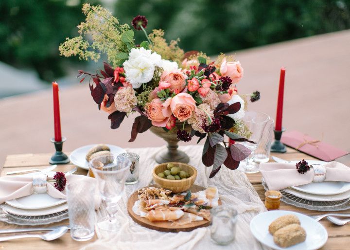 tablescape showing winter wedding colors with red taper candles, bowls of green grapes, white, dishes, and dark burgundy flowers