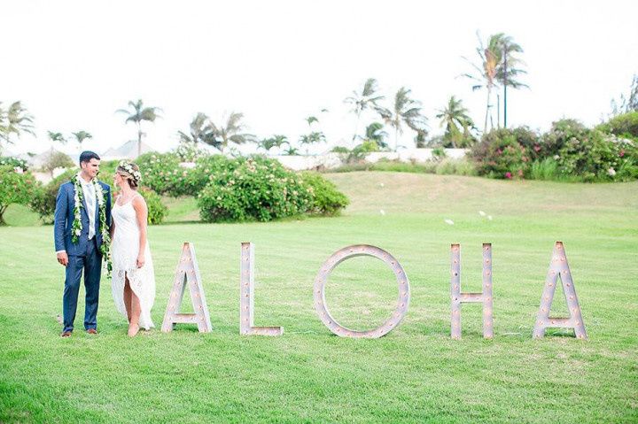 bride and groom smiling while standing next to large marquee letters that spell 