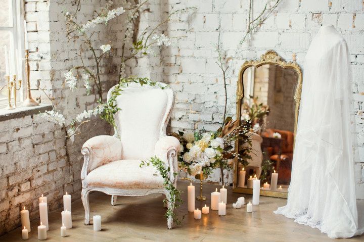 vintage armchair surrounded by white flowers and greenery with candles and wedding dress