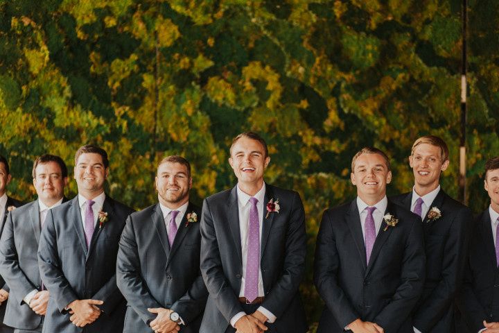 groom wearing navy blue suit and purple tie stands with groomsmen