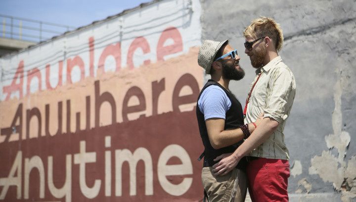 two engaged men hug near a mural in Philadelphia 