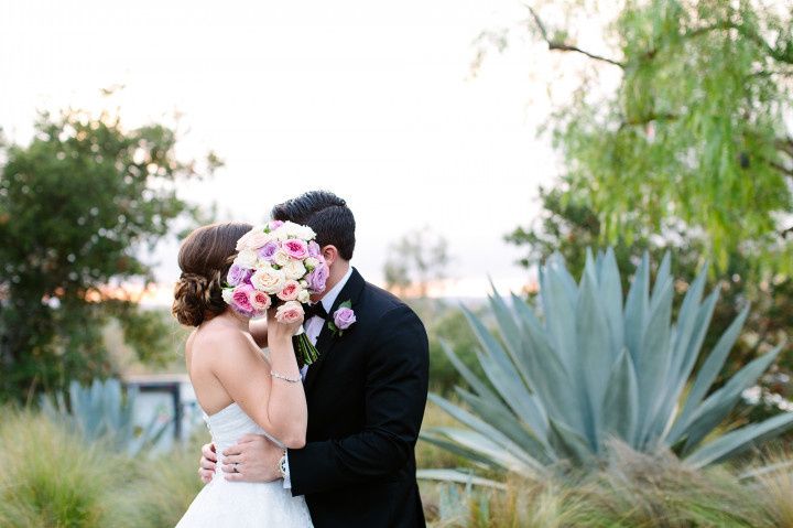 bride and groom kissing behind bouquet 