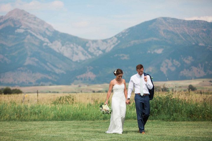 bride and groom walk through green meadow in montana at outdoor wedding with mountain peaks in the background