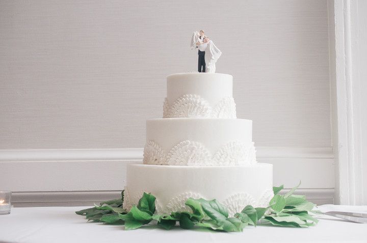 white wedding cake with bride groom topper and greenery at base