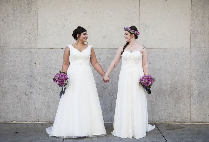 two brides with purple bouquets holding hands