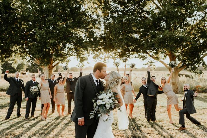 bride and groom kissing with cheering wedding party in background