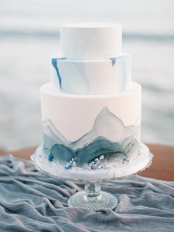 three-tier wedding cake with white fondant and blue watercolor decoration