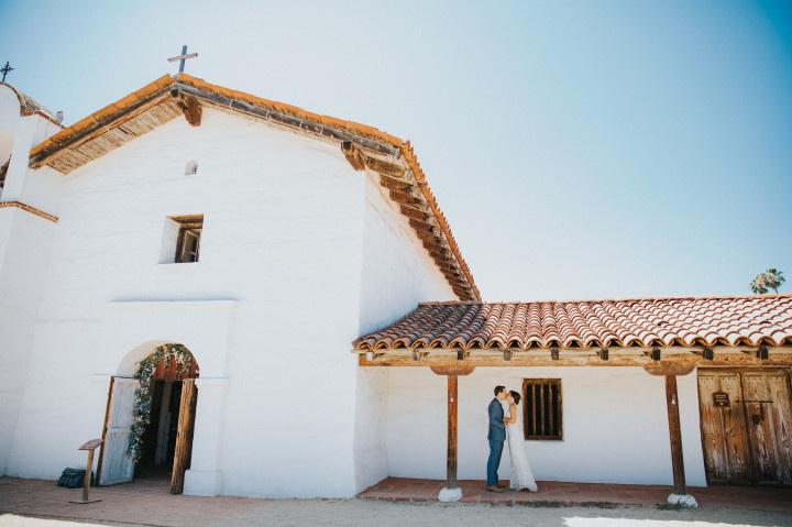 bride and groom pose in front of old mission church in Santa Barbara