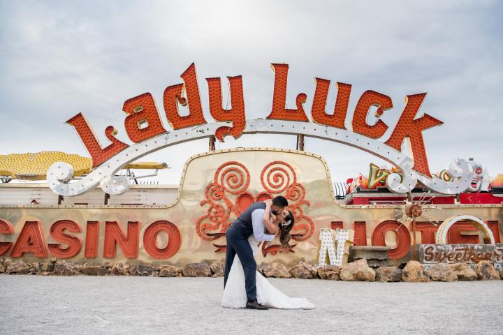 bride and groom pose in front of vintage Lady Luck casino sign at Neon Museum wedding venue in Las Vegas