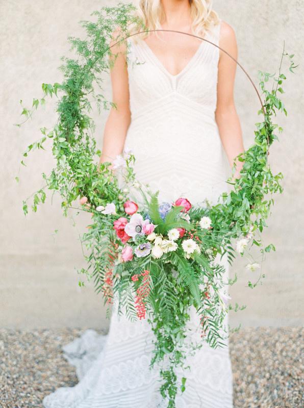 bride holds metal wreath decorated with trailing greenery and pink and white flowers