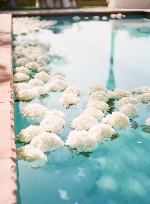 bunches of white hydrangeas floating on in-ground pool at outdoor wedding venue