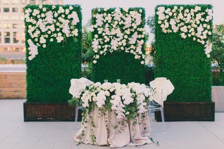 three faux greenery panels decorated with white flowers stand behind sweetheart table at outdoor wedding venue