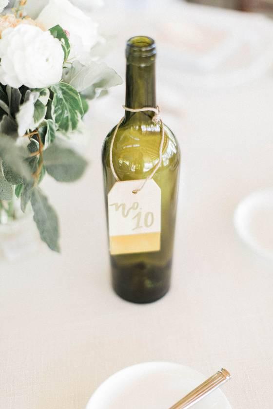 empty green glass bottle with table number card tied around using baker's twine