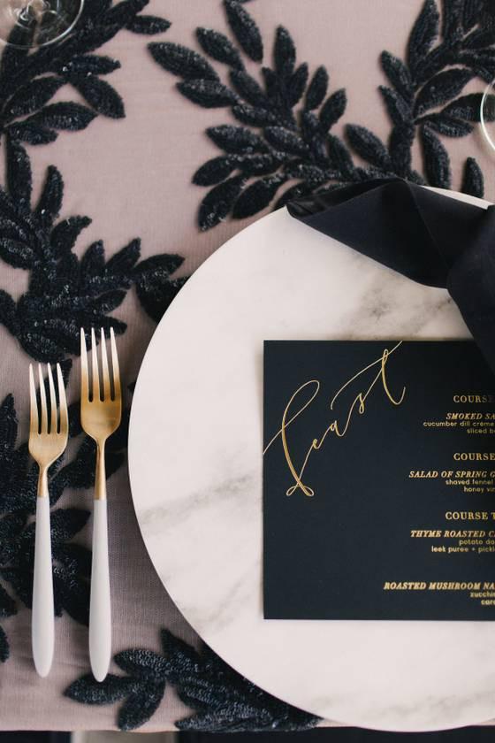 winter wedding colors - close-up of gold and white silverware at a table setting with a black menu on the plate