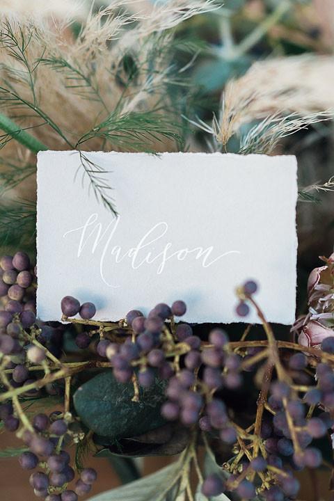 close up of calligraphy escort card on a bed of purple berries