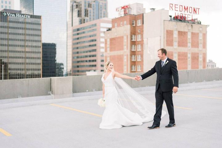 bride and groom pose in wedding attire on rooftop overlooking birmingham alabama skyline