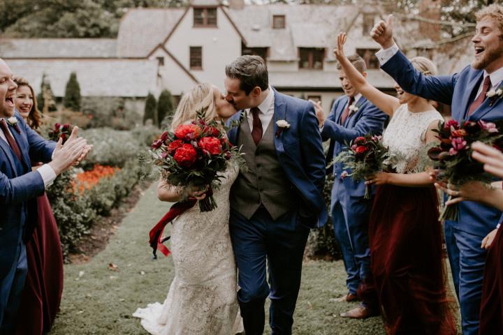 bride and groom kiss as they walk down the aisle and wedding party cheers