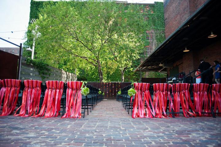 outdoor wedding ceremony with chairs decorated with red streamers