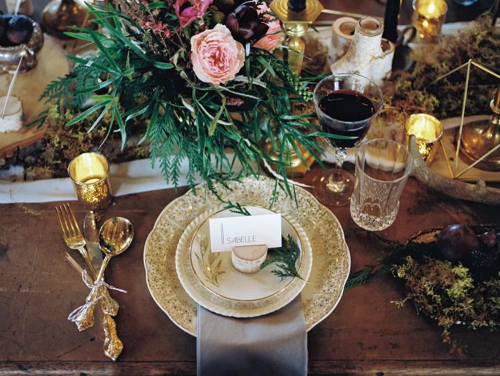 rustic table with vintage gold flecked places gold silverware and outdoorsy centerpiece 