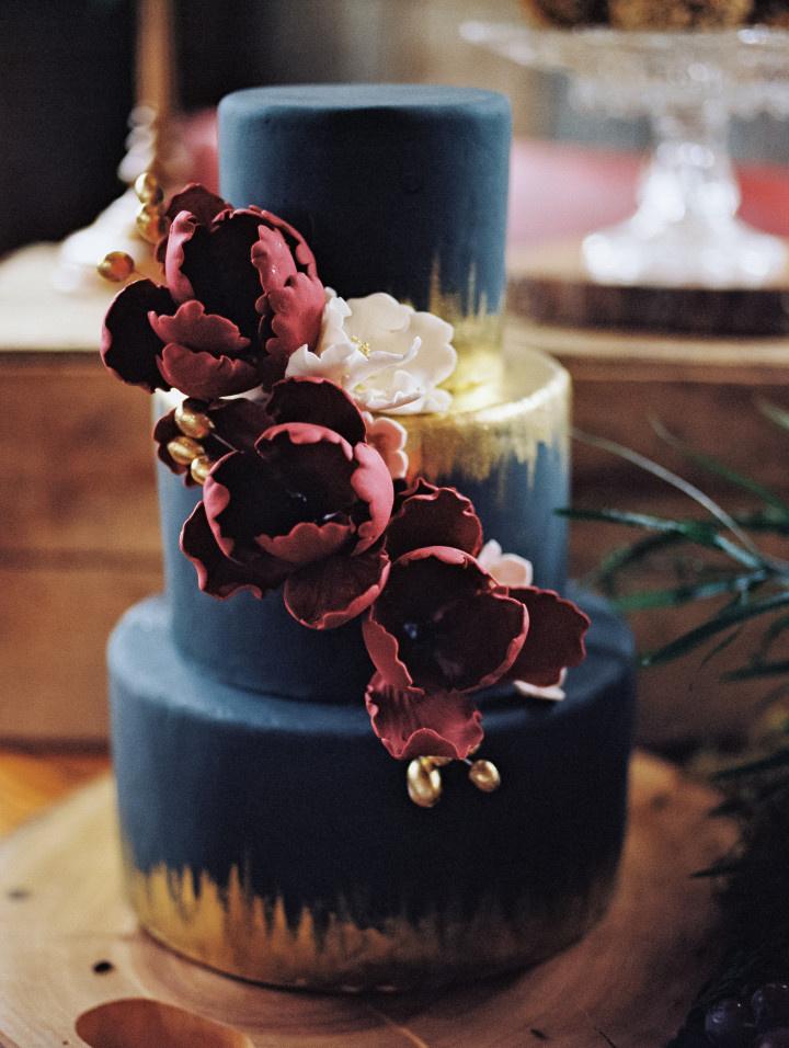 three-tiered navy hued fondant cake with gold accents and cascading florals 