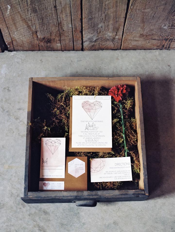 Geometric inspired invitation suite with pink water color displayed in moss filled box 