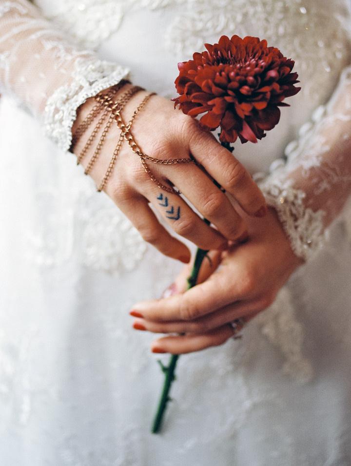 bride with red nails and delicate finger tattoo holding chrysanthemum