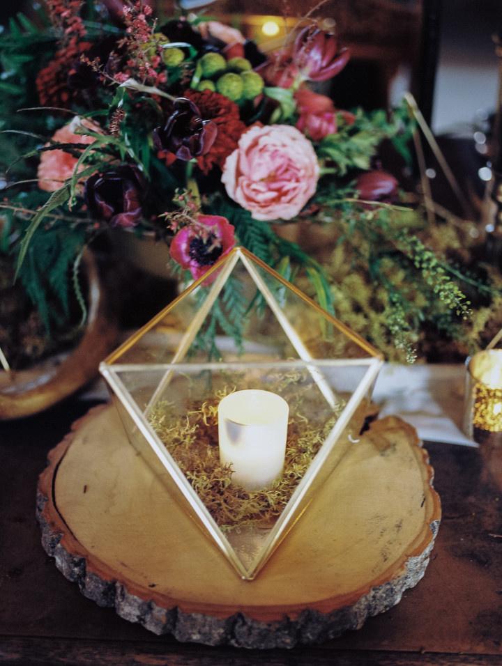 Geometric prism candle holder on wooden slice next to floral centerpiece 