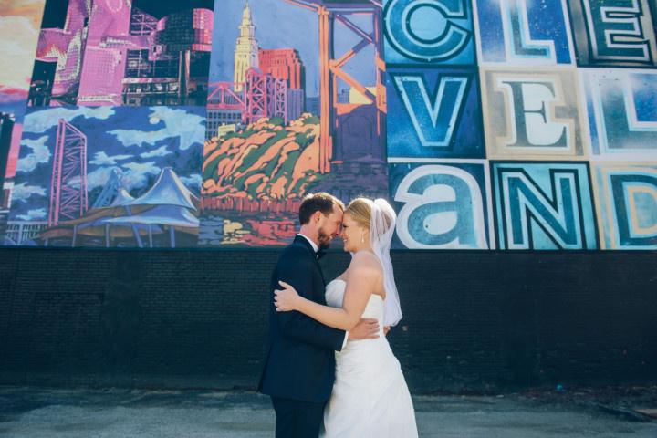bride and groom pose with their wedding party in front of cleveland mural wall