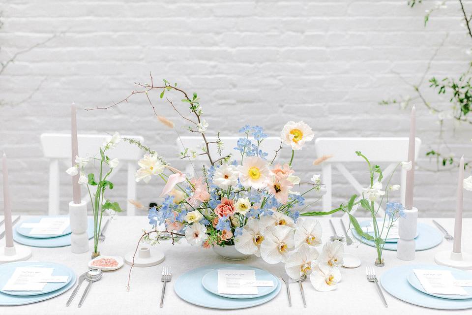 wedding tablescape with centerpiece featuring pastel flowers such as blue delphinium poppies and rose buds