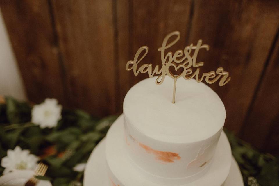 white wedding cake with gold topper that says best day ever