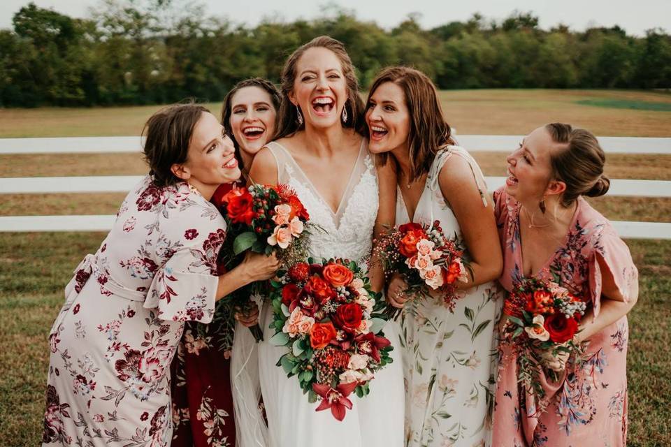 bride stands and laughs with her bridesmaids who are wearing mismatched pink floral print dresses