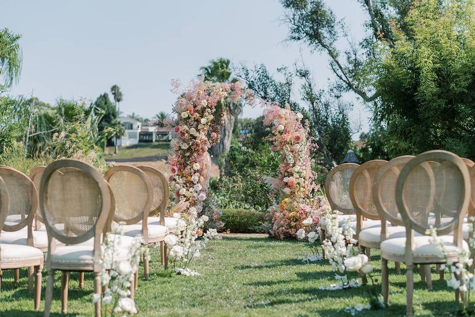 outdoor wedding ceremony in garden with cane back chairs and romantic blush pink floral arch at the altar