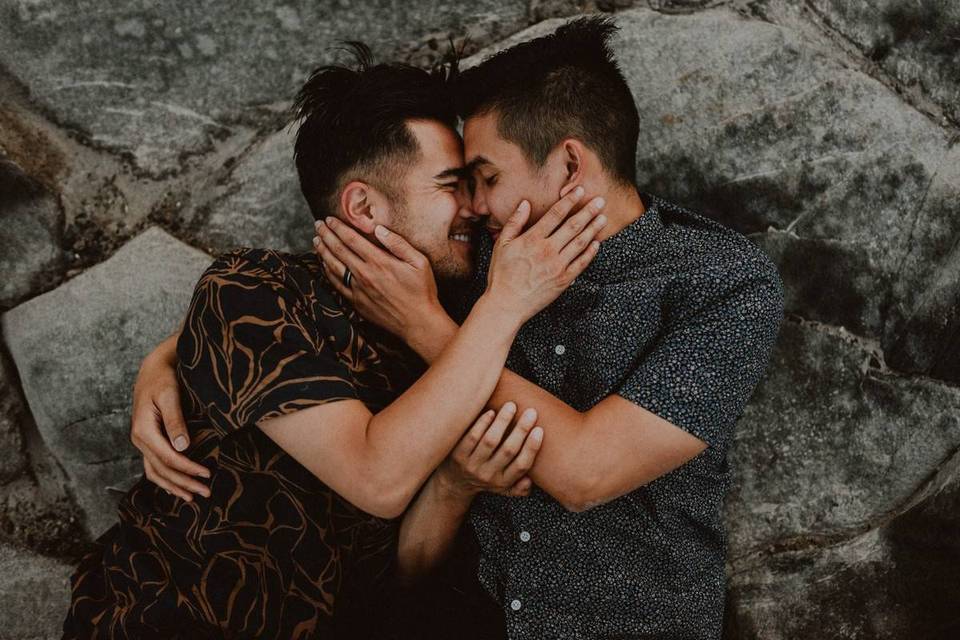 LGBTQ+ couple two men hugging closely with arms wrapped around each other and foreheads touching looking into each other's eyes with hands on cheeks