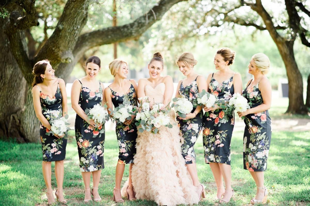 Bride wearing wedding gown in the middle of bridesmaids wearing floral midis in woodland setting