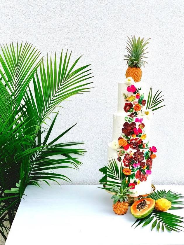three-tier beach wedding cake decorated with bright icing flowers and palm leaves