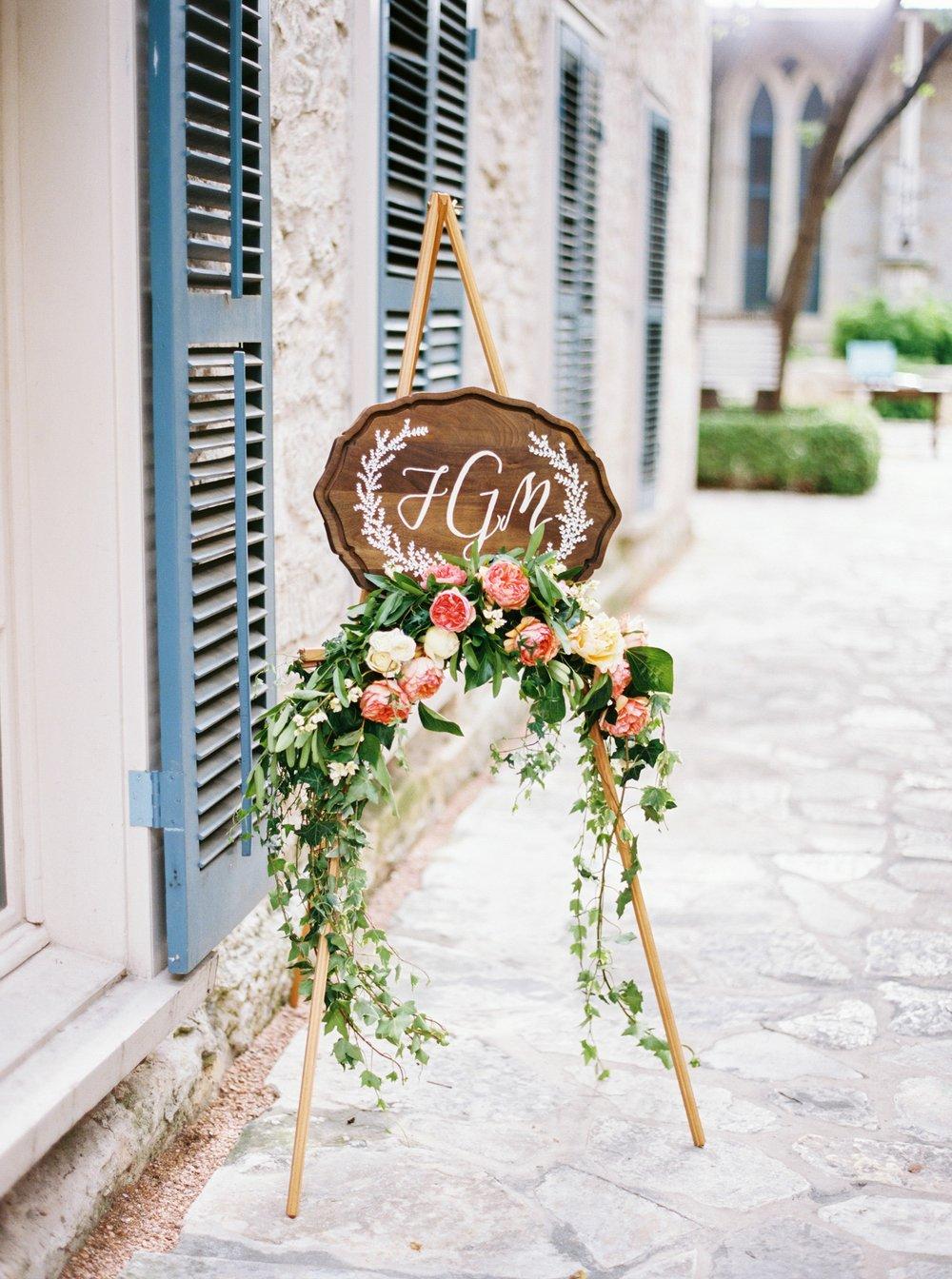 wooden sign featuring couple's monogram in white calligraphy is decorated with pink garden roses and eucalyptus