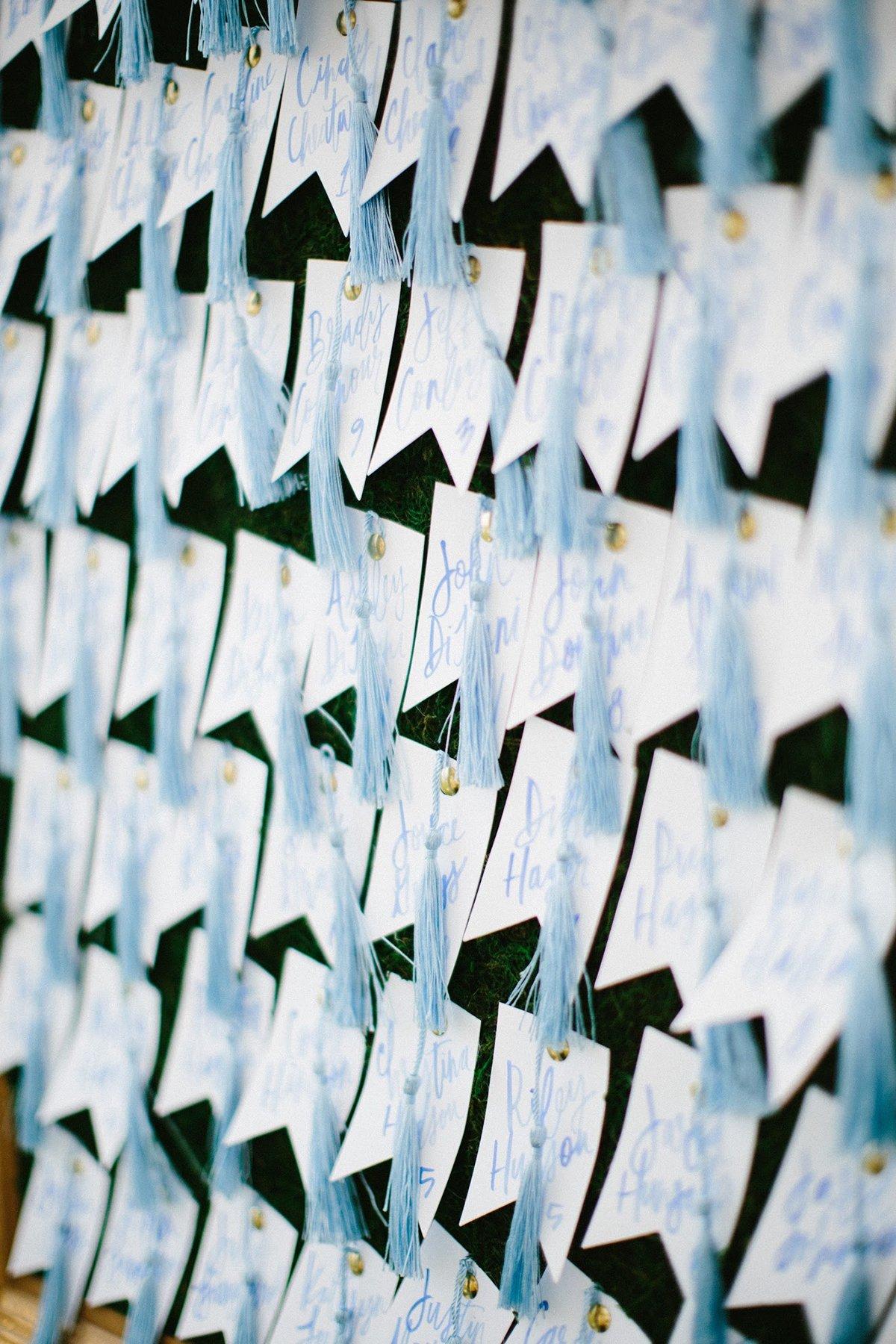 wall of wedding escort cards shaped like mini bunting flags decorated with light blue tassels