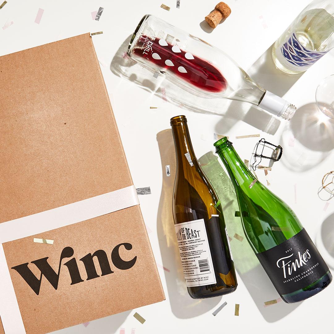Коробка доставки Winc рядом с пустыми винными бутылками на столе с конфетти