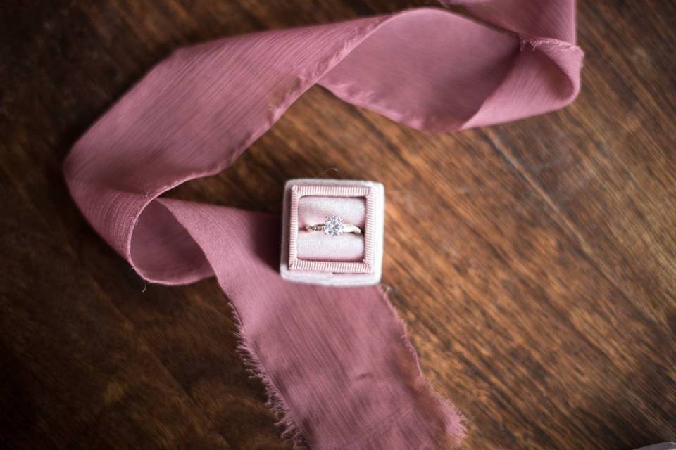 overhead photo of engagement ring in pink velvet square ring box on wooden table