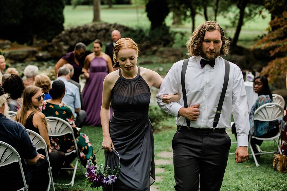 Bridesmaid and groomsman walking together with guests in their seats wearing fall wedding atitire