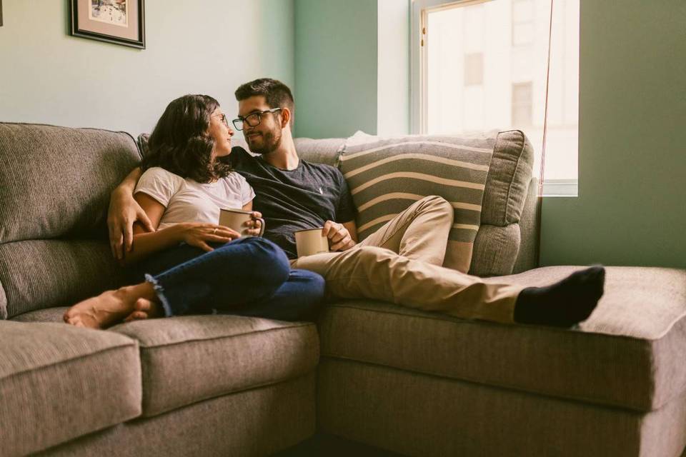 engaged couple holding coffee mugs and sitting on couch