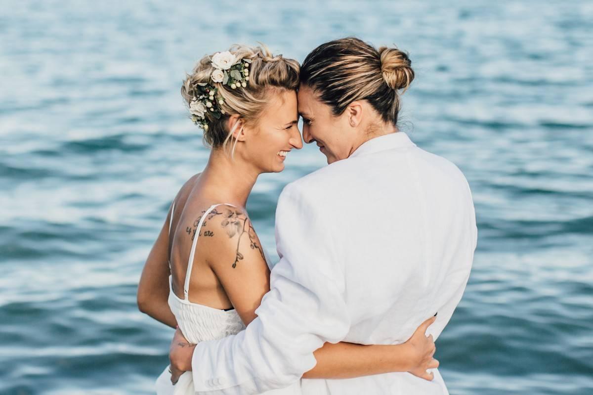 two brides pose on the beach and sweetly look into each other's eyes