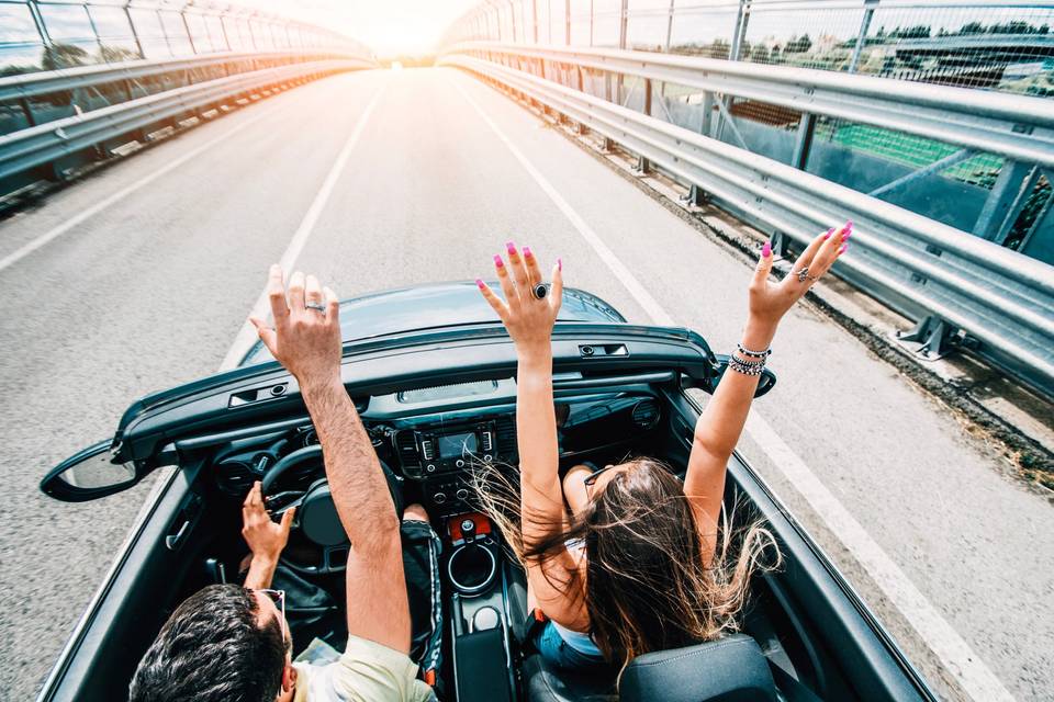 man and woman riding in convertible with their hands in the air