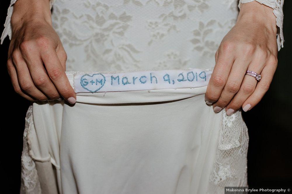 bride lifts up hem of wedding dress skirt embroidered with initials in a heart and wedding date in blue thread