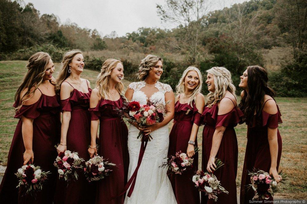 Bride and bridesmaids posing outside with bridesmaids wearing burgundy