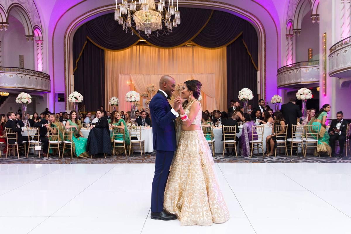 Indian bride and groom during first dance with groom wearing navy blue tuxedo and bride wearing white and gold lehenga